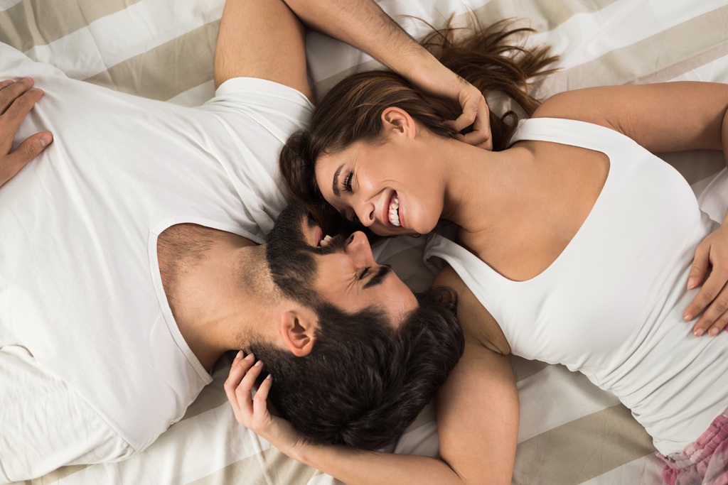 Woman and man laying head to head in a bed looking into each others eyes and smiling lovingly